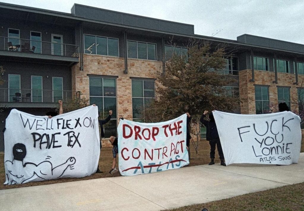 A picture of 3 banners in front of an office building. The first one on the left reads "We'll Flex on Pavetex" with a drawing of a masked person flexing their arm. The second reads "Drop the Contract Atlas" the third reads "Fuck you Lonnie, Atlas sucks"