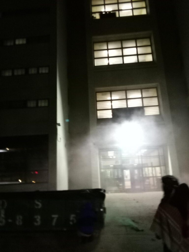 smoke fills the air in front of the jail, lit by one fluorescent light above the door